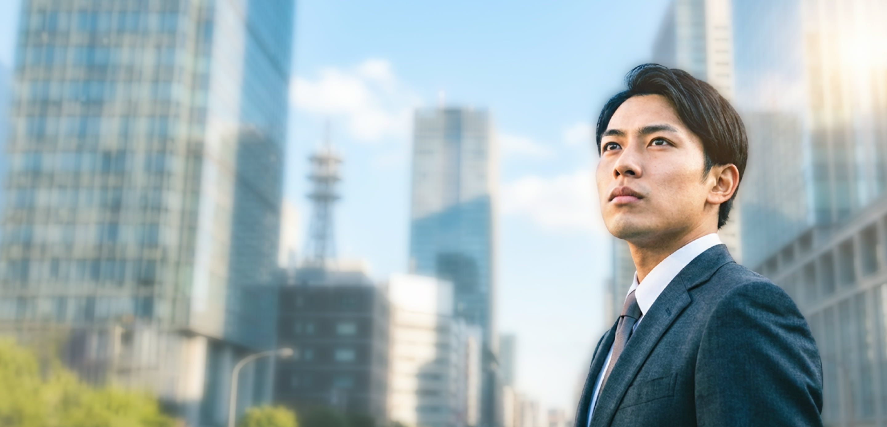 オフィス街で空を見上げるスーツ姿の若い男性の写真